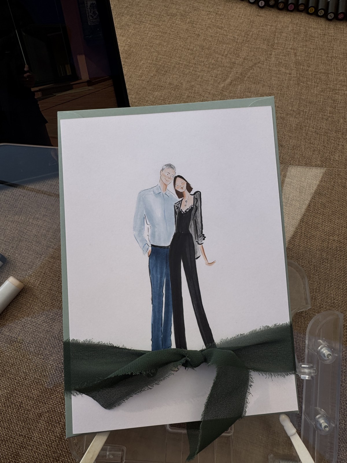 Ilustración de una pareja con sobre verde salvia y un lazo de tul